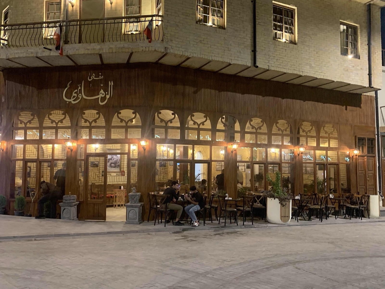 The warmly lit facade of Al-Zahawi Coffeehouse in Baghdad at dusk, with people at outdoor tables.