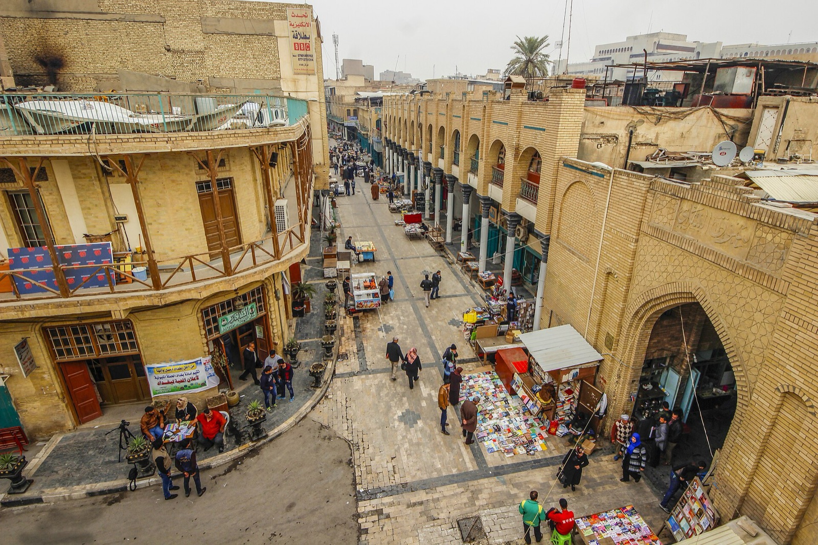 Books spread on the pavement of Mutanabbi Street in Baghdad, with people browsing and buildings on both sides.