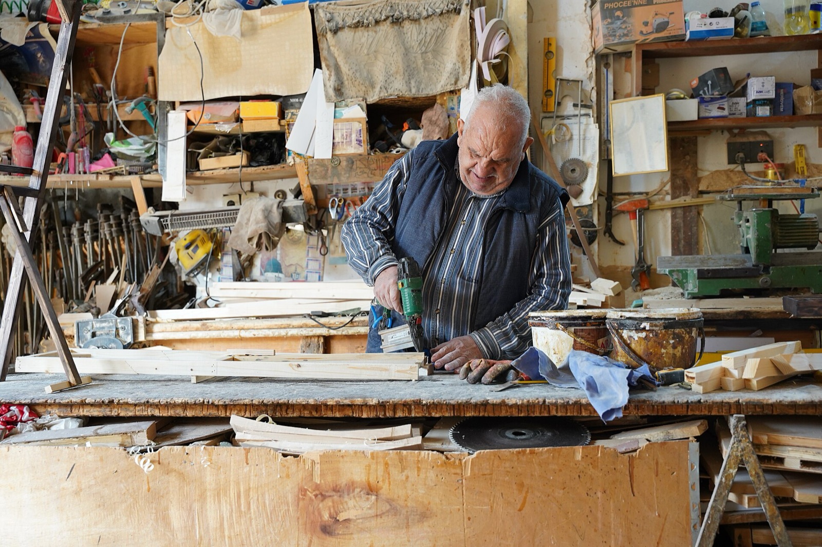 A carpenter working at a bench in a cluttered workshop in Kirkuk's Quriya Market.